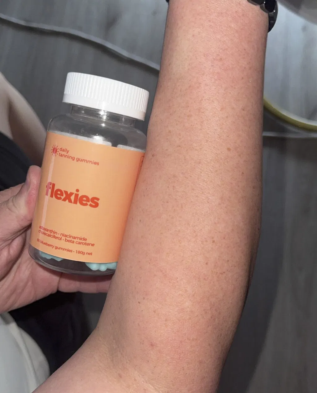 Flexies customer Scott S. holding Sun Kissed Tanning Gummies next to his arm showing a subtle warm glow on fair skin