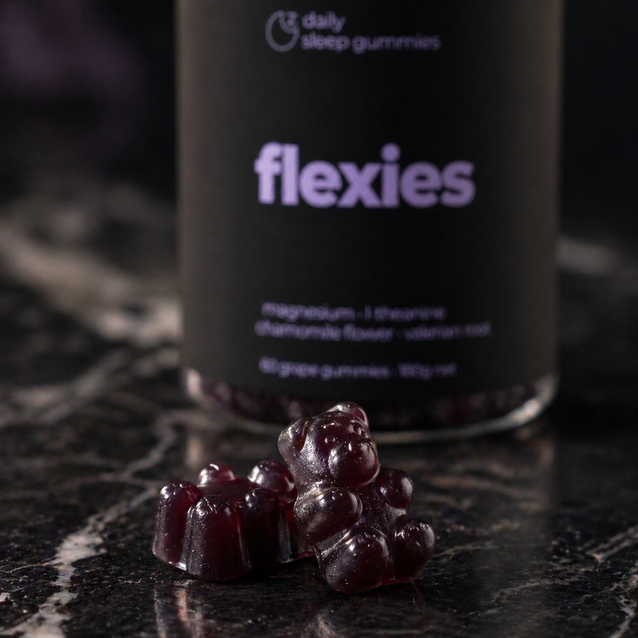 Close-up of two grape Flexies sleep gummies in front of the daily sleep gummies bottle on dark marble